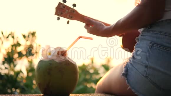 年轻的嬉皮士女孩在美丽的热带海滩日落时演奏尤克莱尔吉他4K泰国视频的预览图