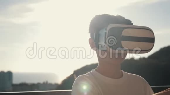 日落时快乐的男孩戴着虚拟现实眼镜玩电子游戏快乐的微笑看着VR眼镜和虚拟现实眼镜视频的预览图
