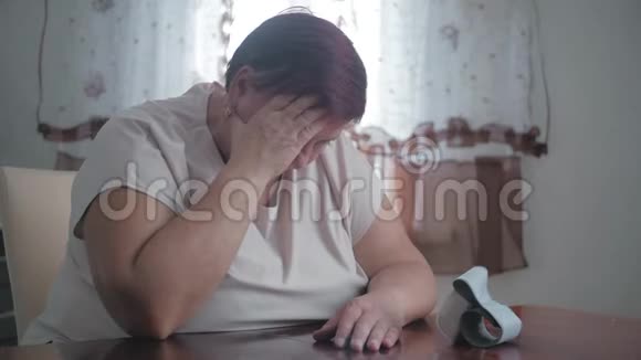 成熟的肥胖妇女坐在桌旁用数字血压计测量压力高级女性负责照顾视频的预览图