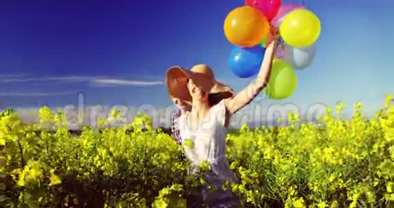 浪漫的一对夫妇手里拿着五颜六色的气球在芥菜田里奔跑视频的预览图