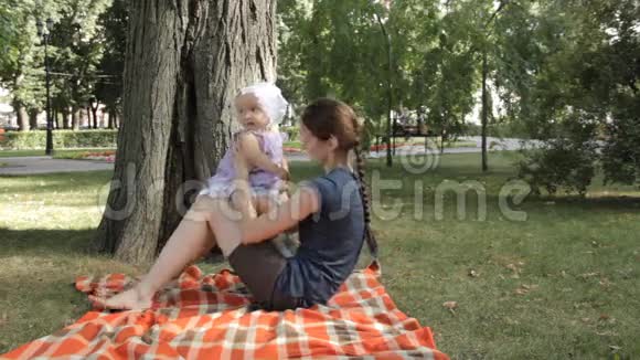 一个小女孩坐在草地上铺着毯子的年轻保姆的膝上视频的预览图