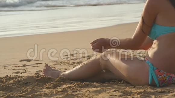 美丽的年轻女子坐在沙滩上的金色沙滩上在暑假旅行中放松女孩视频的预览图