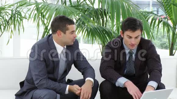 两个商人坐在沙发上用笔记本电脑视频的预览图