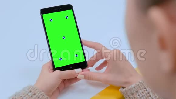 女人看着黑色智能手机带空绿色屏幕视频的预览图