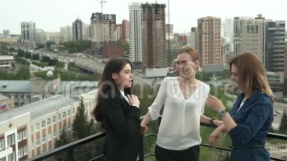 女朋友在午休时愉快地聊天三个迷人的女孩在屋顶上闲聊城市的景色视频的预览图