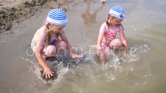 两个女孩在海滩上泼水在炎热的夏日里双胞胎倒着水孩子们的笑声和好心情视频的预览图
