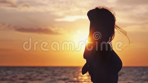 带着长长的头发戴着太阳镜在多风天气中缓慢地在海滩上享受日落的迷人女孩视频的预览图