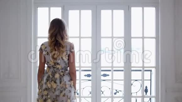 金发女孩穿着一件明亮的长裙子穿着一扇大窗户视频的预览图