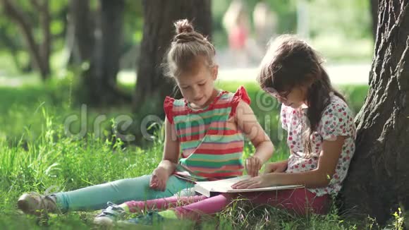 两个小女孩在树下享受晴天和看书姐姐给妹妹读一本书视频的预览图