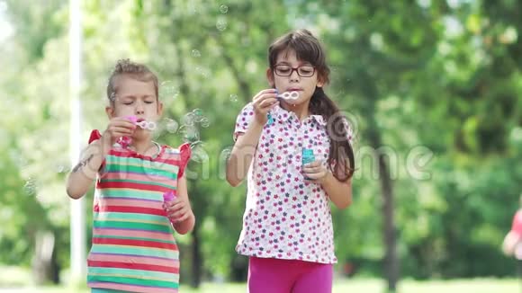 快乐的孩子在春天公园吹肥皂泡两个小女孩在夏天公园玩得很开心慢动作视频的预览图