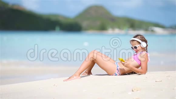 小女孩在海滩上用耳机听音乐视频的预览图