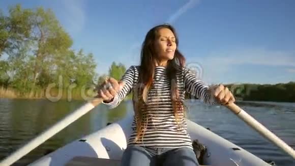 年轻的快乐混合种族女孩划船充气船与木桨在湖上高清慢动作生活方式录像视频的预览图