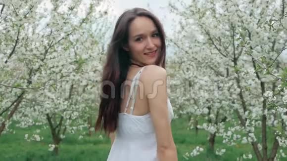 春天的时尚肖像一位美丽快乐的年轻女子穿着白色连衣裙棕色长发奔跑享受花香视频的预览图