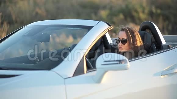 美丽的女孩穿着皮夹克的长发戴着太阳镜的皮裤在日落时分下车视频的预览图
