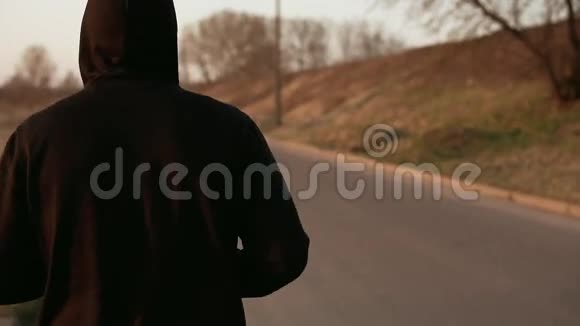 户外日落时孤独的跑步者穿着黑色带帽毛衣慢动作视频的预览图