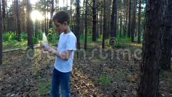 小男孩从瓶子里喝水日落时分在森林里的夏夜视频的预览图