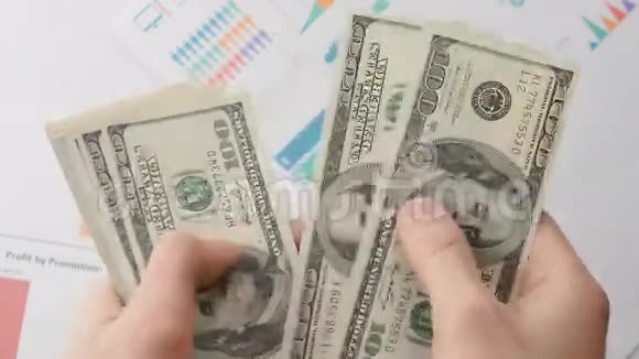 一个商人的特写他的手在一张桌子上数着一百美元的钞票视频的预览图
