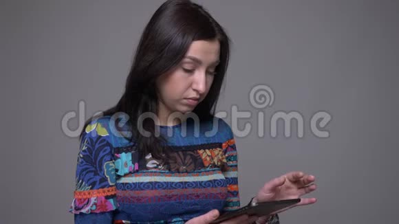 一张成年白人黑发女性在平板电脑上发短信和观看背景隔离摄像头的特写照片视频的预览图