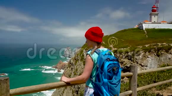 背着背包的女人可以欣赏灯塔附近的海洋海岸视频的预览图