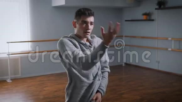 穿着灰色套头衫和黑色裤子的英俊的男舞者在教室的中央有感情地跳舞青年视频的预览图