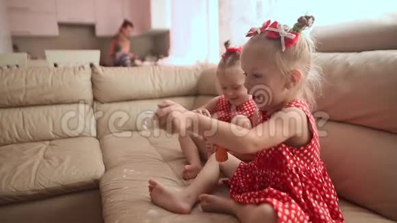 两个小双胞胎姐妹穿着迷人的红色连衣裙光着脚坐在房间里兴高采烈地吹着肥皂泡视频的预览图