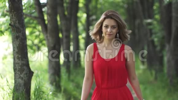 一个穿着红色裙子的漂亮年轻女人的性感肖像女孩沿着绿色的小巷走着微笑着慢慢慢慢视频的预览图