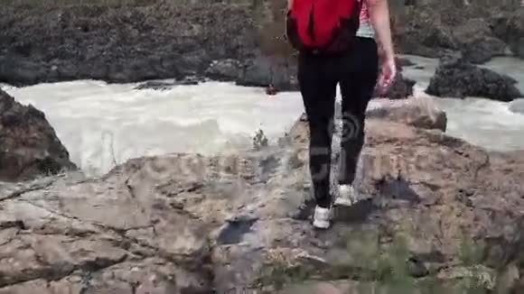 女孩旅行者在一条山河的岩石上山崖边的年轻女子游客视频的预览图