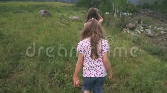 孩子们沿着草地走两个小女孩的旅行者走过一片靠近山河的田野视频的预览图