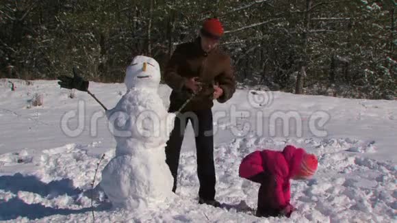 爸爸和小女儿在森林附近的草地上堆雪人视频的预览图