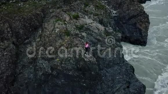 空中飞行一位背着背包的女旅行者站在山上的悬崖边上欣赏着令人惊叹的景色视频的预览图