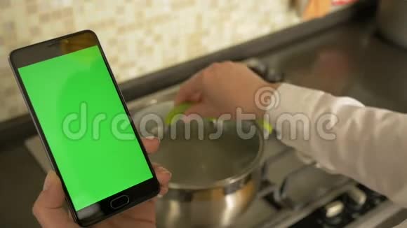 一个女人拿着一台绿色屏幕的智能手机煮汤视频的预览图