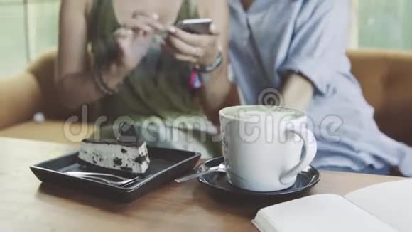 两个女性朋友使用智能手机桌子上有蛋糕和一杯拿铁视频的预览图