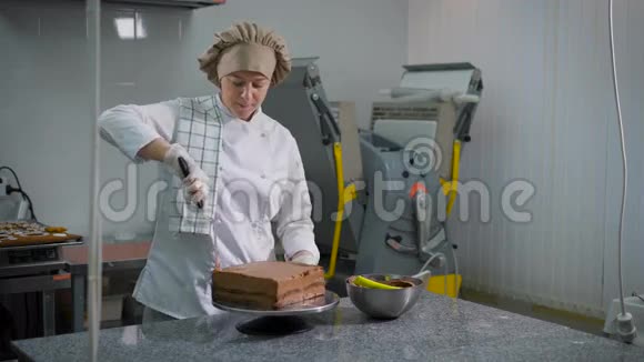 一个面包店的专业厨房里一个带铲子的糖果在刚出炉的蛋糕上铺上巧克力奶油碗视频的预览图