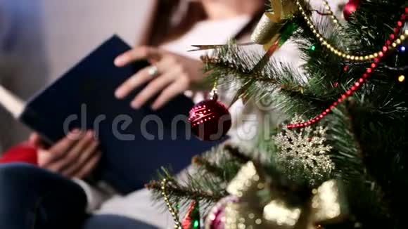 美丽的年轻女士坐在圣诞树附近的椅子上看书视频的预览图