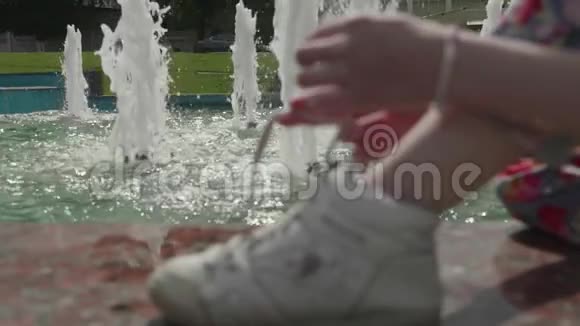 坐在喷泉附近的女孩和系运动鞋慢镜头视频的预览图