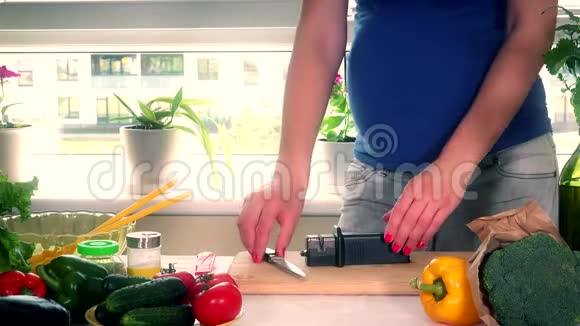 孕妇的肚子和桌子上磨刀的手视频的预览图