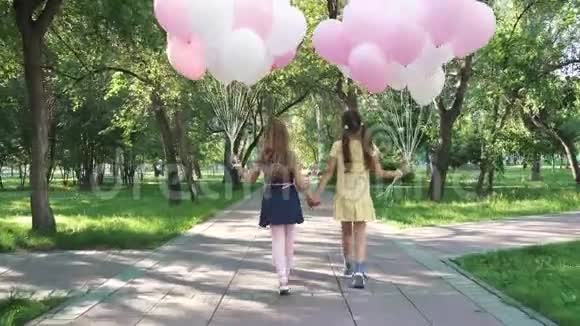 孩子们拿着气球穿过夏天的公园两个小女孩拿着很多五颜六色的气球从视频的预览图