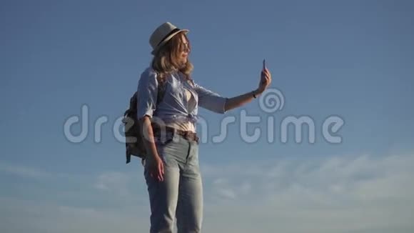女孩旅行者在手机相机上自拍年轻的女人是个带背包的笨蛋戴太阳镜戴帽子的女孩视频的预览图