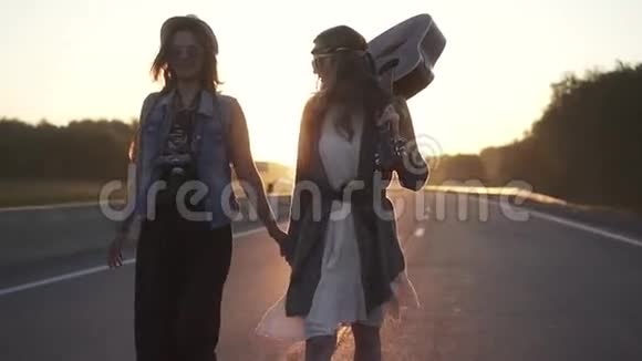 两个嬉皮士女孩在黎明时沿着高速公路走慢动作视频的预览图