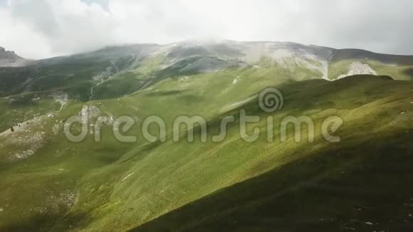 空中观景台飞越一片绿草如茵的岩石山在美丽的云彩中飞过高山视频的预览图
