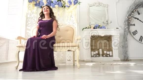 穿着晚礼服的年轻女子穿着紫色衣服坐在豪华的室内沙发上视频的预览图