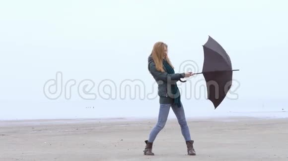 在雾蒙蒙的海滩上漂亮的少女迎风打伞视频的预览图