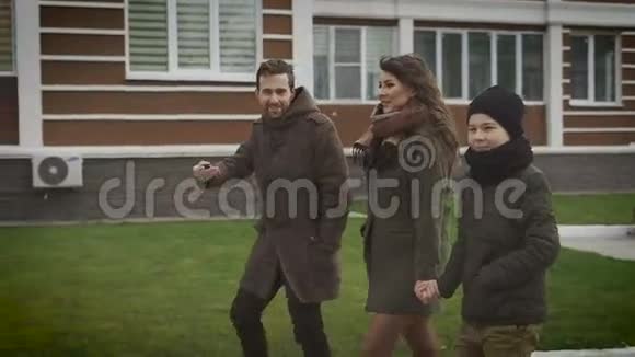 快乐的年轻家庭一起度过周末三个穿暖和衣服的快乐的人在街上一起散步视频的预览图