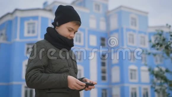 院子里站着一个男孩在人行道上他穿着一件夹克一顶黑色帽子脖子上戴着一条围巾他玩你的视频的预览图