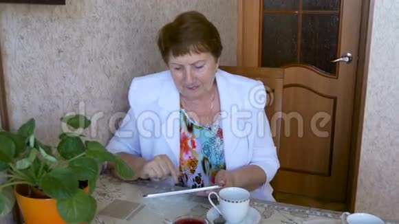 老年妇女在餐桌上喝茶在平板上看照片视频的预览图