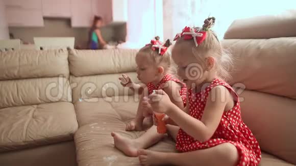 两个小双胞胎姐妹穿着迷人的红色连衣裙光着脚坐在房间里兴高采烈地吹着肥皂泡视频的预览图