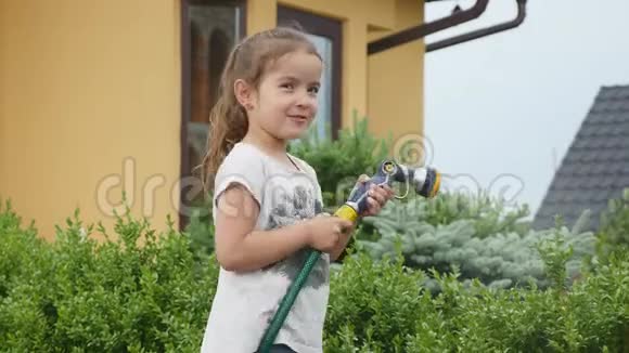 可爱的小女孩拿着一根水管在给草坪浇水时摇动它视频的预览图