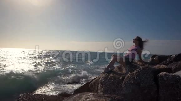 女孩坐在岩石上看着海浪视频的预览图
