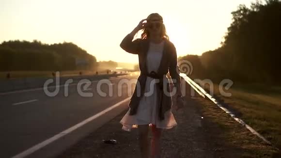 女孩嬉皮士在朝阳的照耀下走在路上黎明时一位年轻女子的肖像视频的预览图