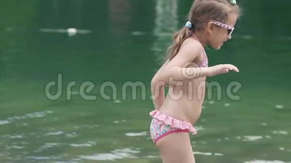 孩子在河里洗澡做滑稽的脸小女孩穿着泳衣和太阳镜在海边享受一天视频的预览图